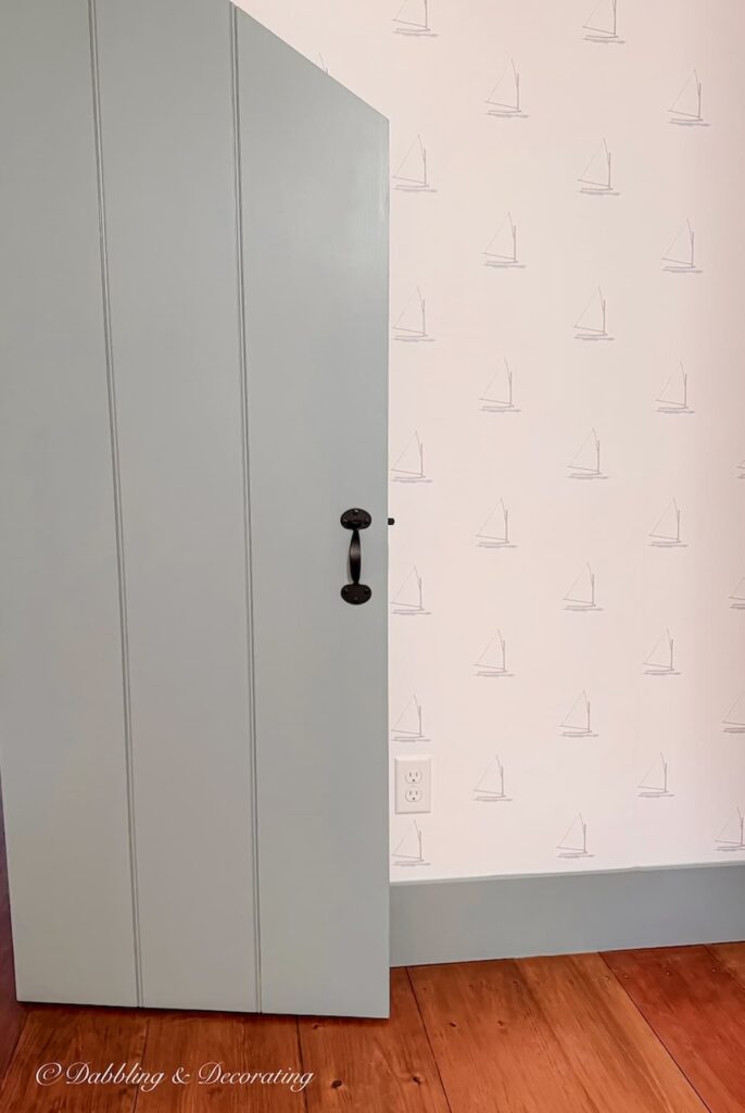 Custom historic paint color in blue-gray on colonial style latch door next to Sailboat wallpaper in attic guest bedroom in old colonial home in Maine.