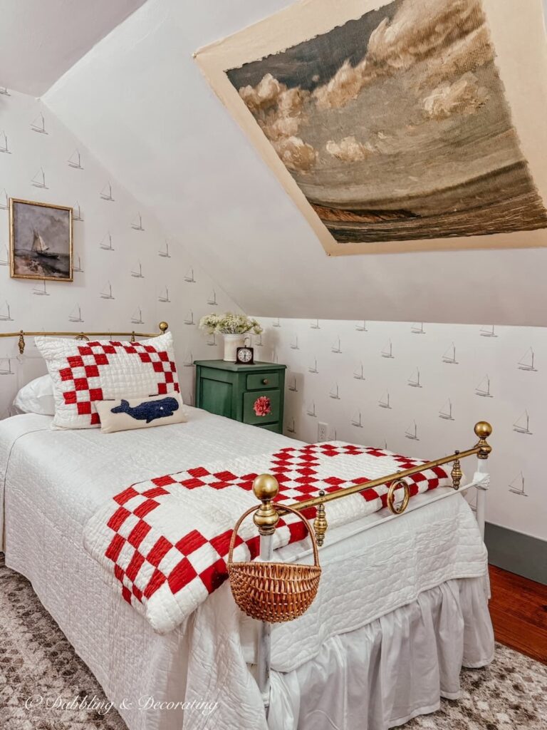 Small vintage styled guest bedroom in attic with sloped ceilings and a hanging thrifted coastal inspired tapestry on the sloped ceiling above the bed. 
