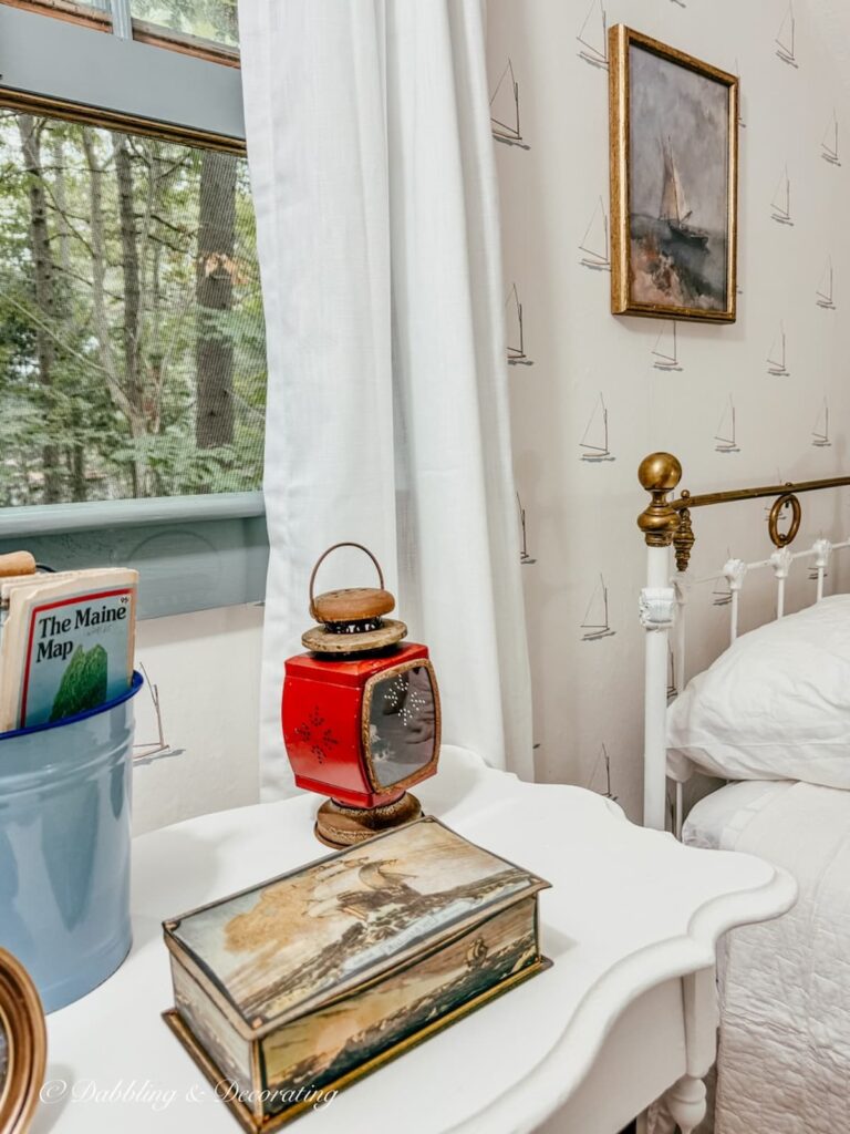 Small bedroom in attic with coastal thrifted bedroom ideas with red lantern on side table, coastal print on sailboat wallpaper and antique bed.