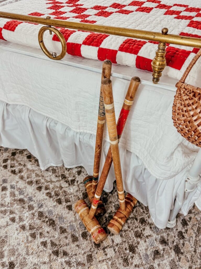 Three thrifted vintage croquet mallets leaning up against an antique wrought iron bed with brass details in thrifted bedroom ideas.