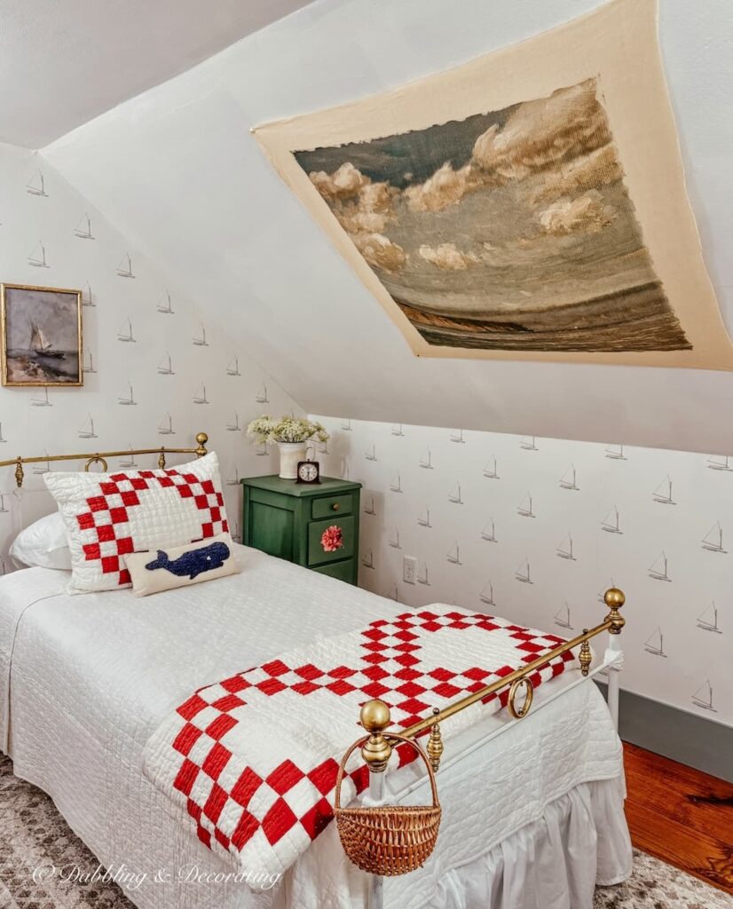 Vintage-inspired tapestry with a coastal scene displayed on slanted ceilings in attic bedroom with antique twin wrought iron bed.