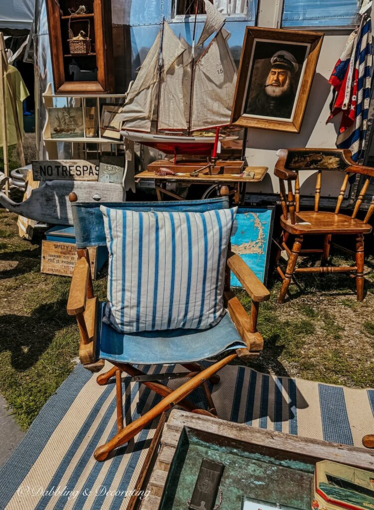 Vintage Booth with blue and white nautical display outdoors at Vintage Bazaar New England in Mystic, CT with sailboats, nautical chairs, rugs, paintings, and more.