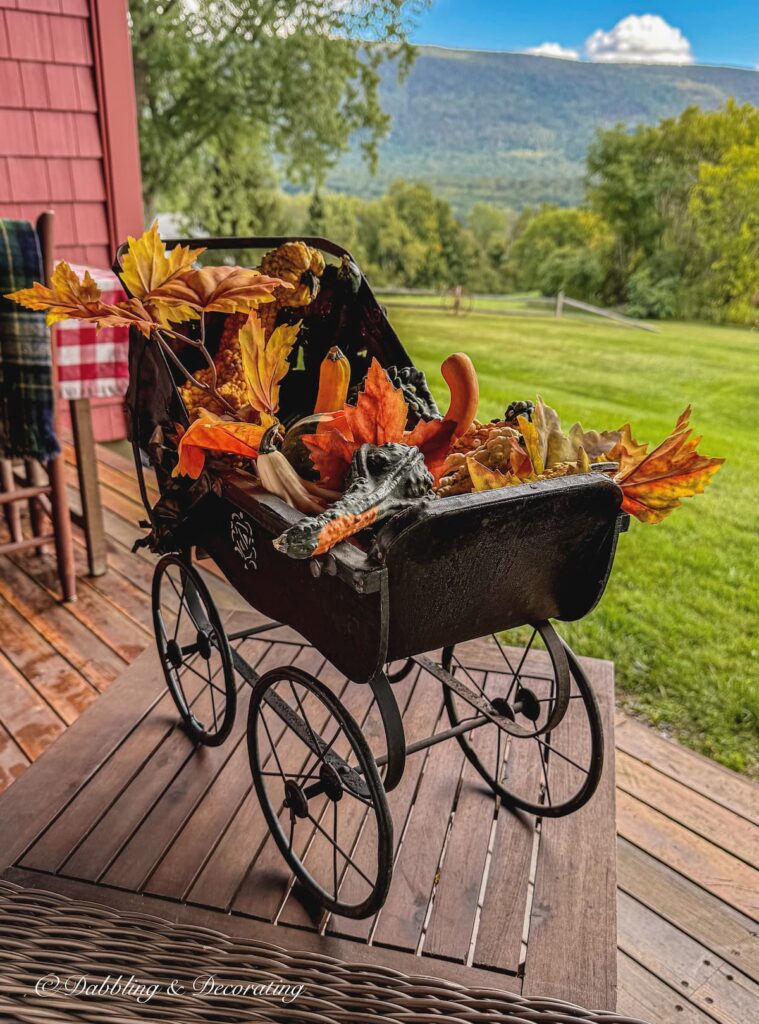 Antique black doll carriage filled with gourds for vintage Halloween ideas on a porch with mountain views.