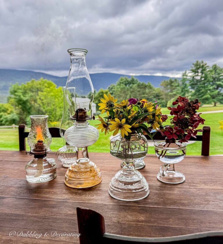 Six antique oil lamps on display on fall porch vintage table with flowers and chimney's with mountain views.