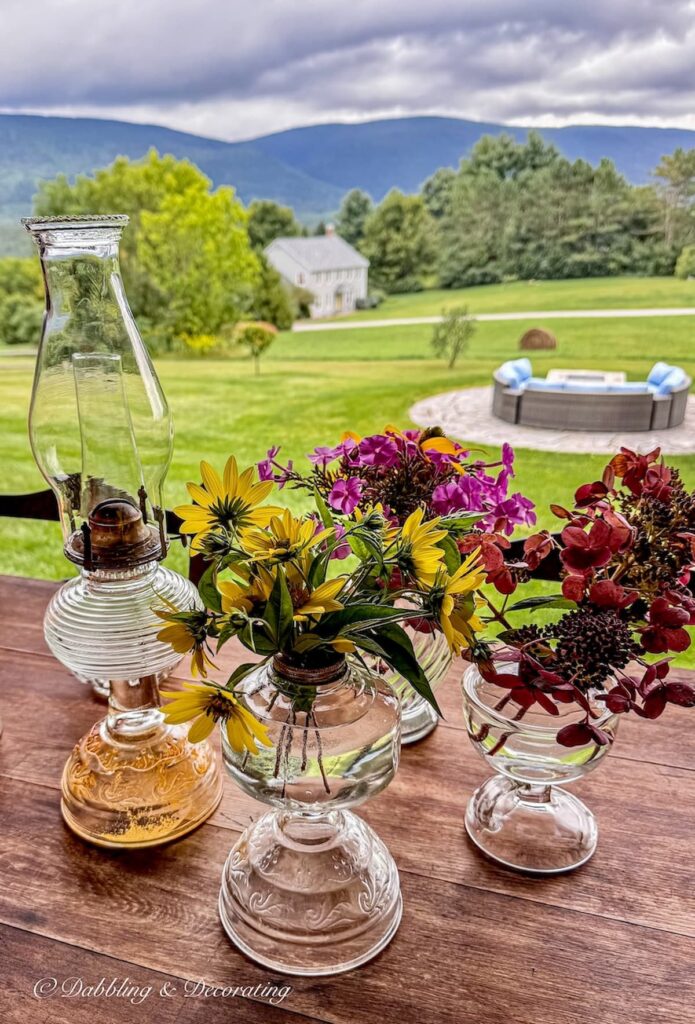 Antique oil lamps styled on an outdoor porch table in the mountains with flowers.