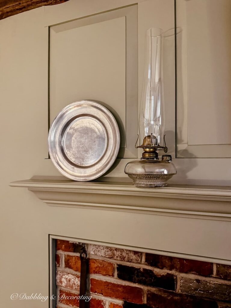 Antique oil lamp next to a pewter plate on old colonial mantel over brick fireplace with Nantucket Gray Hearth.