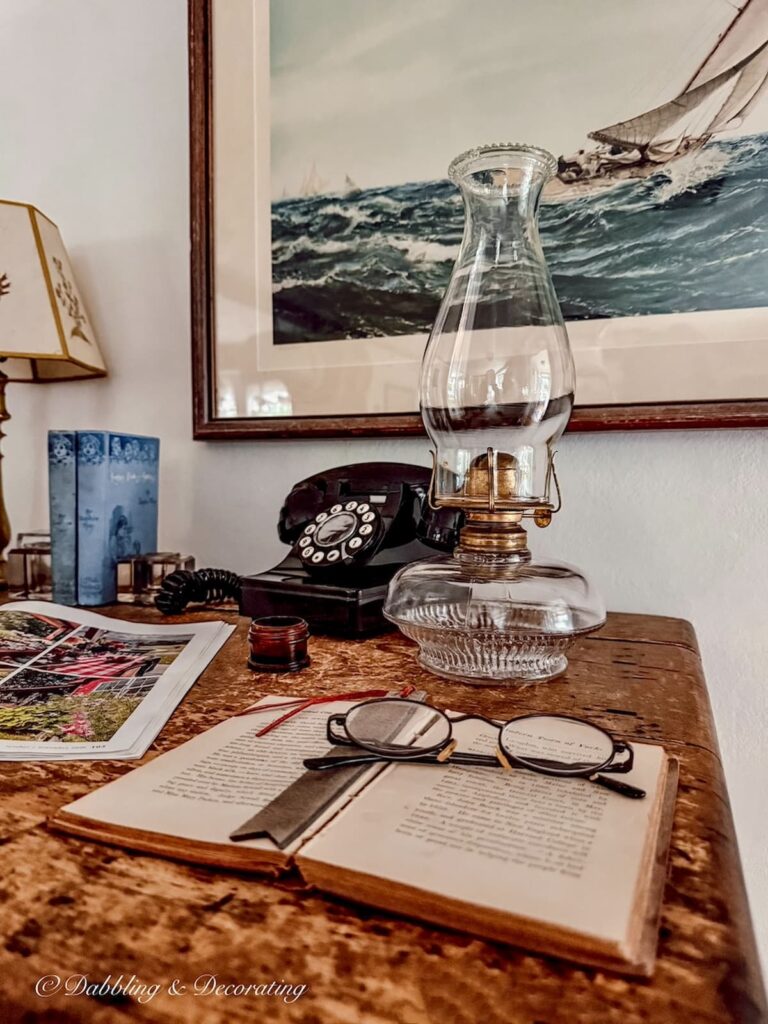Antique desk styled with an antique oil lamp, open vintage book, old telephone and coastal wall art.