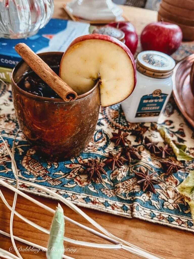 Vintage copper mug with apple slice and cinnamon stick on table for fall styling.