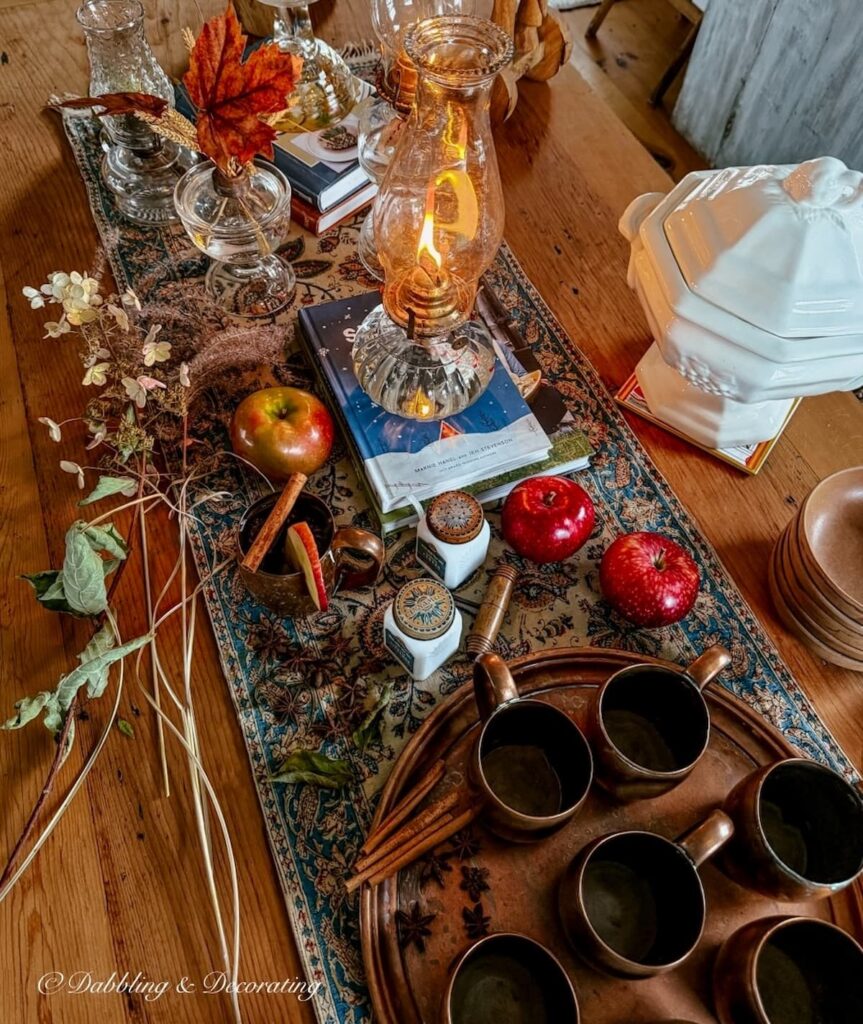 Fall table styled with vintage finds; oil lamps, vintage copper, apples, foraged branches, old spice jars, blue and orange textile, soup tureen and wooden bowls.