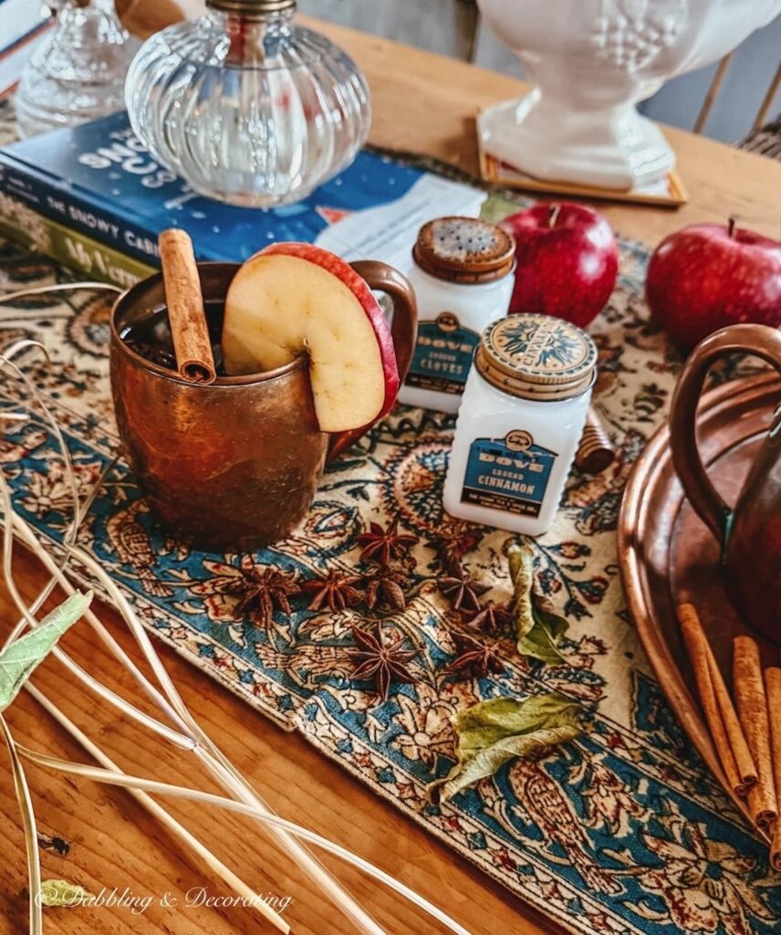 Wooden table set with vintage copper, old spice jars, antique Iranian textile, antique oil lamps, spices, and apples in fall home decor.
