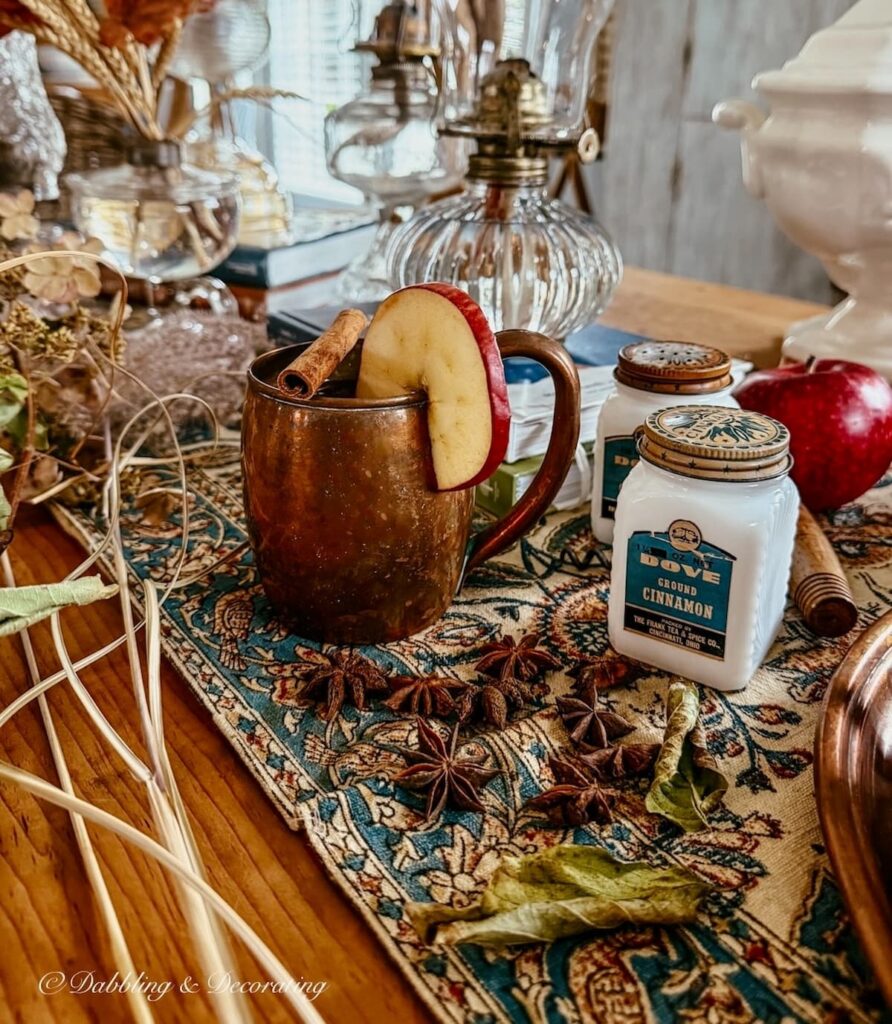 Fall table setting with vintage copper mugs, old spice jars, gathered foraged branches, antique runner, oil lamp collection and more in fall home decor ideas.