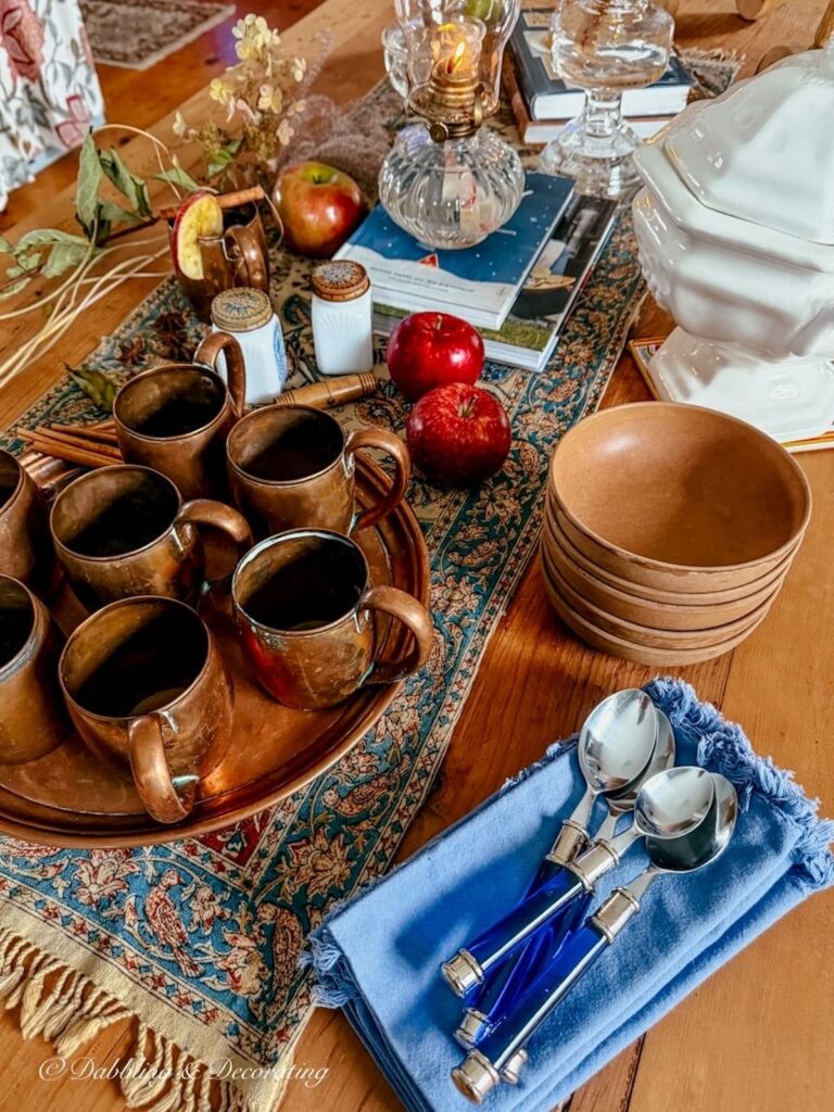 Vintage copper mugs styled with apples and fall finds on an antique textile in a vintage-inspired scullery.