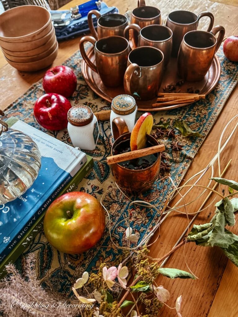 Vintage fall table set with vintage copper, apples, blue and brown textile, apples, oil lamps on stacked books, and wooden bowls in fall home decor ideas.