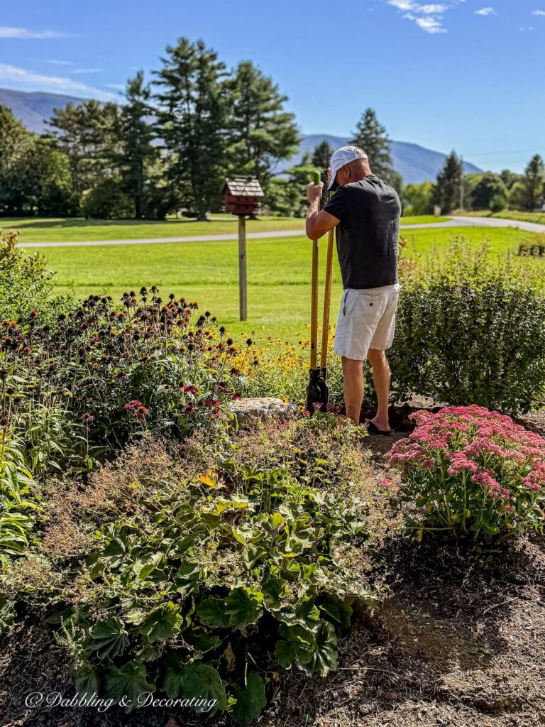 Man digging a hole with a hole digger in fall garden with mountain views.