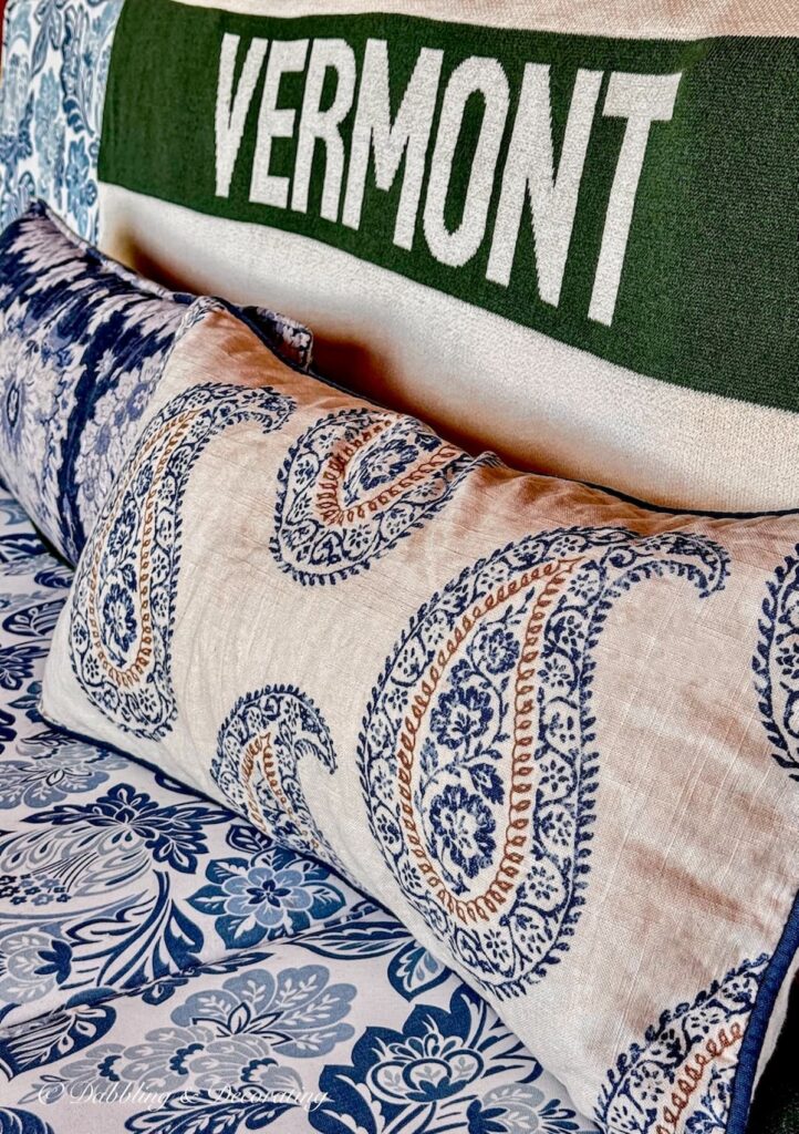 Vermont green and cream striped blanket from The Vermont Country Store with VERMONT written paired with blue and brown mixed patterned pillows on all weathered furniture on colorful fall porch.