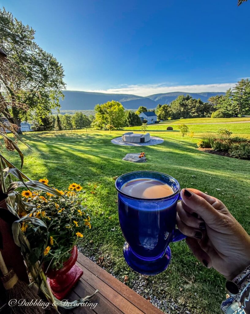 Blue coffee mug in hand toasting to the mountains and colorful fall porch decorating in early morning.