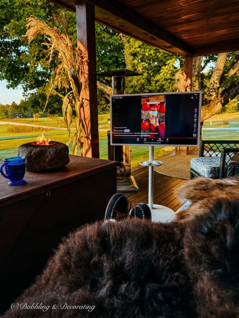 Cozy on the porch under a Luxe Rare Sheepskin with portable television, tabletop fire on colorful fall porch.