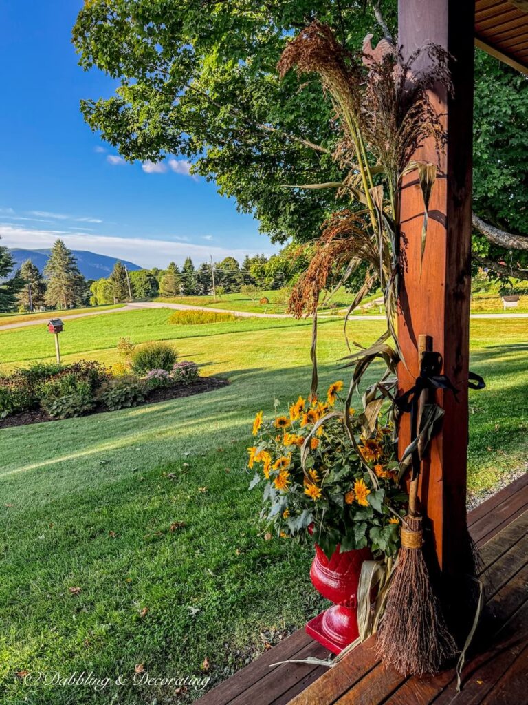 Colonial red planter on colorful porch in the mountains with false sunflowers and corn broom stacks.