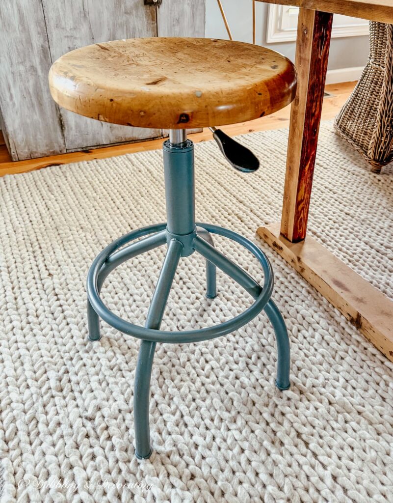 Vintage drafting stool restored with blue-gray paint on white rug next to a scullery wooden table.