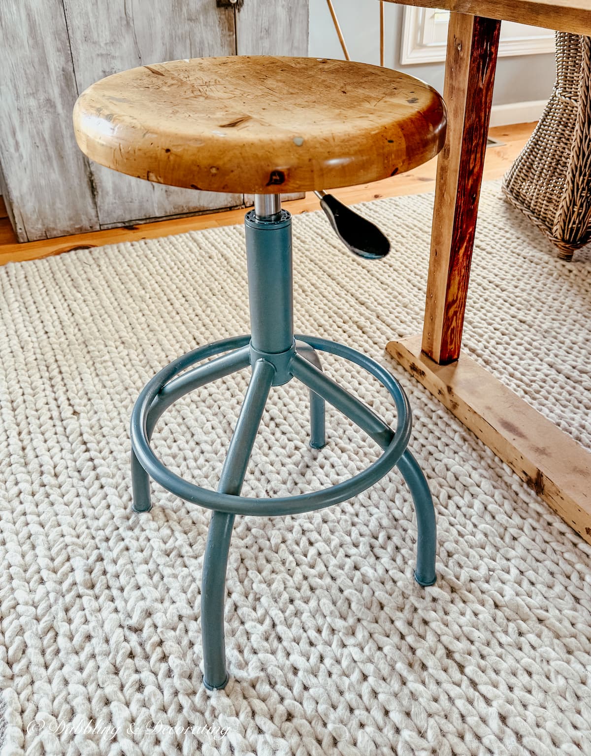 Vintage drafting stool restored with blue-gray paint on white rug next to a scullery wooden table.