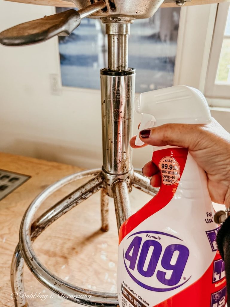409 Cleaner in spray bottle in hand spraying onto antique drafting stool metal.