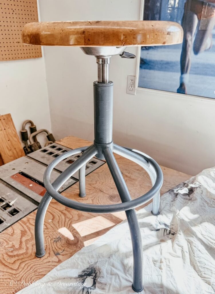 Rusty antique drafting stool restoration with first coat of blue-gray paint color on garage workbench.