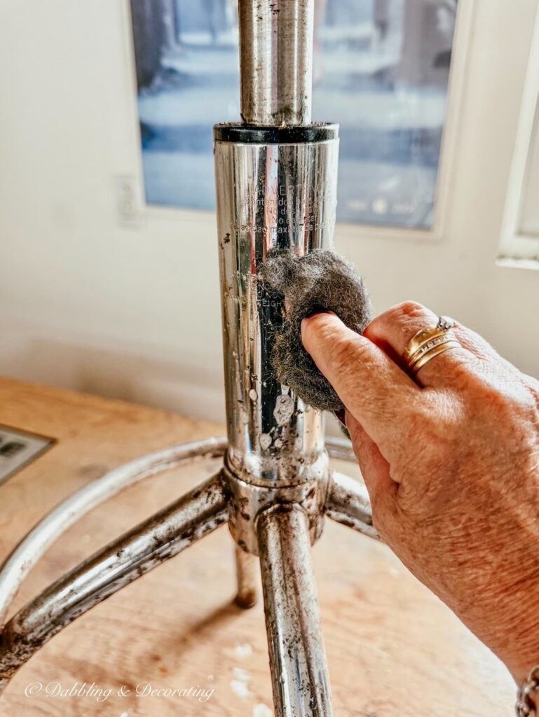 Bottom of antique drafting stool with hand and steel wool rubbing and cleaning the degreaser.
