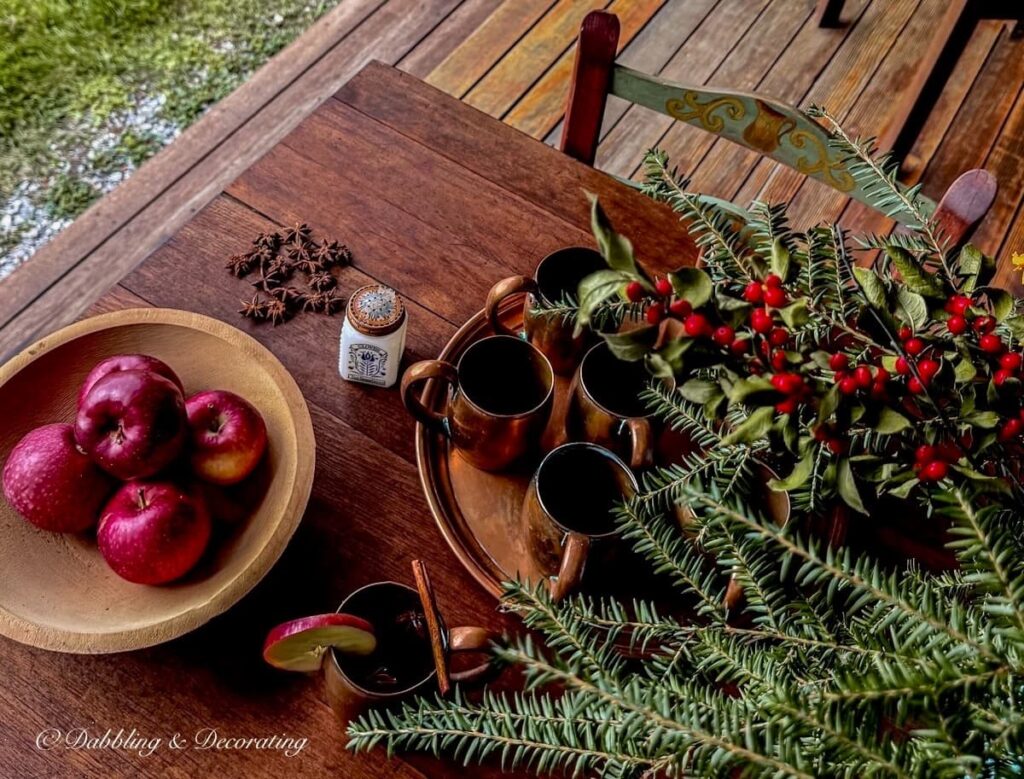 Outdoor vintage wooden table on covered porch with wooden bowl filled with apples, foraged fall arrangement and vintage copper tray and mugs gathered.