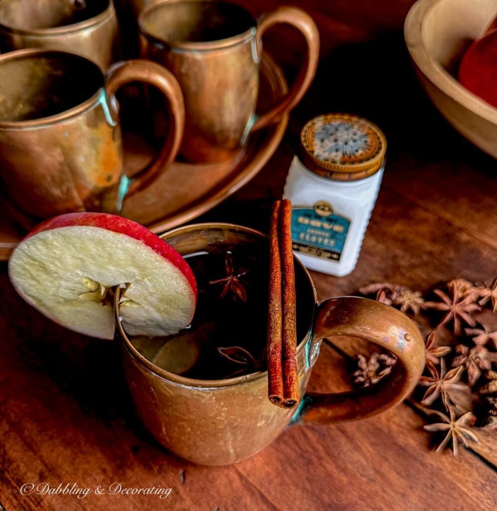 Fall moody vintage copper mug vignette with apple, cinnamon stick, spices and star anise on old wooden table.