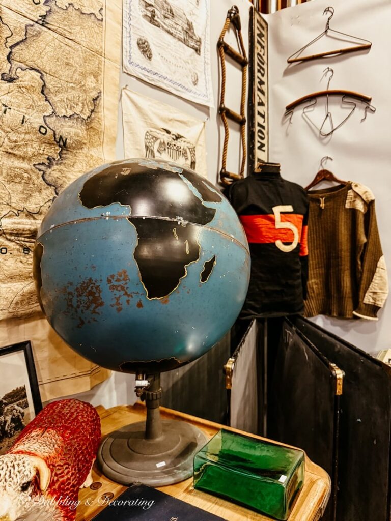 Antique blue oversized globe and varsity sweater on mannequin with world maps in antique booths at Taconic antiques Fair.