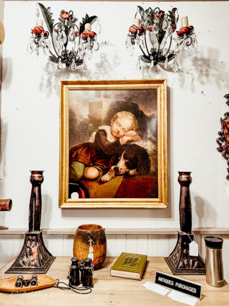Antique painting beautifully displayed on wall with sconces inside High-End Antique Booths.
