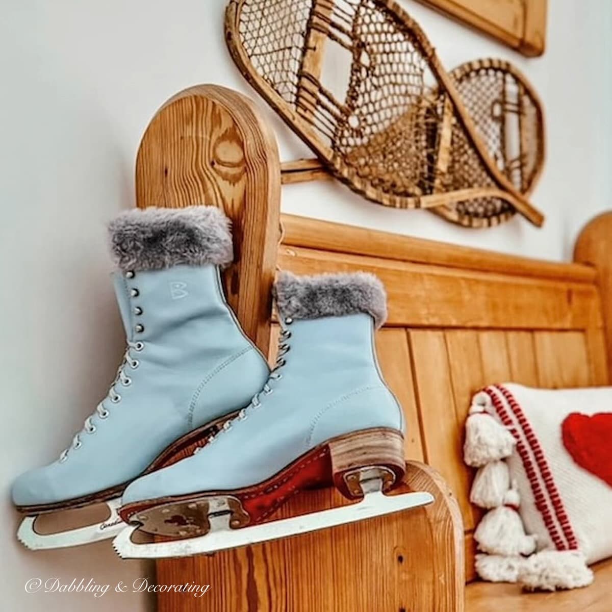 Blue vintage Canadian Flyer women's ice skates draped over an antique church pew in home's entryway with Vintage snowshoes on wall and heart pillow on bench for Valentine's Day decoration.