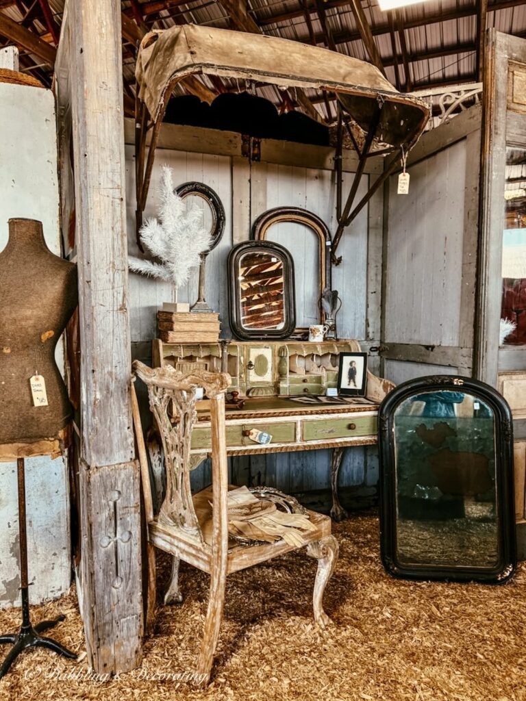 Antiques in a vendor booth with mannequin, carriage cover, chair, desk and more at Country Living Fair.