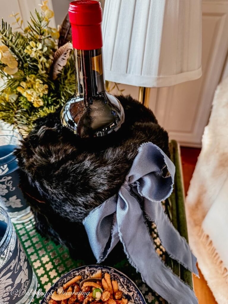 How to dress up a wine cover with a black fluffy hand muff and blue bow on a beverage cart with a bottle of wine in it.