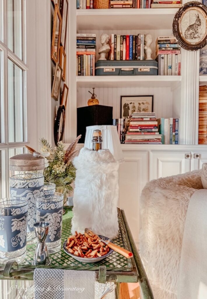 Vintage bar cart with vintage Jeannette barware and a bottle of wine with a white Amazon hand muff as the cover in front of built-in bookshelves with eclectic style.