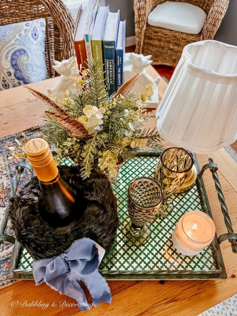 Antique green tray on wooden table with a bottle of a wine with a black vintage hand muff cover, lit candle two green wine flutes and a lamp styled for entertaining.