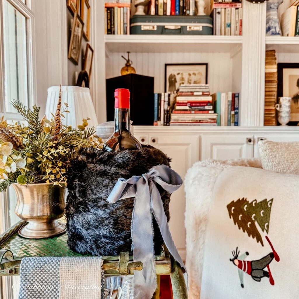 Thrifted black vintage hand muff with blue bow being used as a wine cover on a bar cart in a cozy winter styled corner.