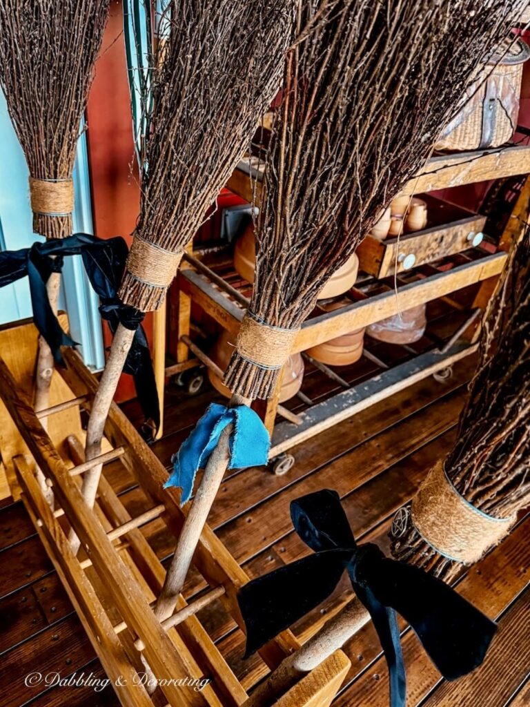 Four witches brooms with blue and black velvet bows in an old ski rack on front porch for Halloween decorations.