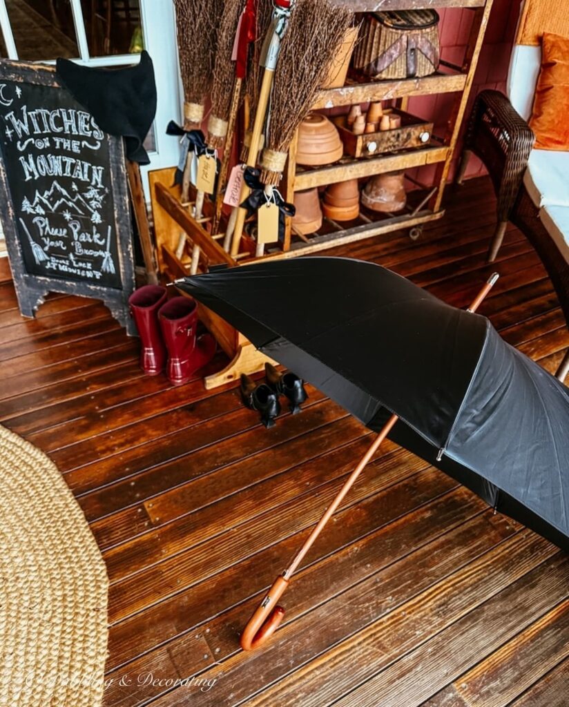 Black umbrella next to a witch's broom parking and Halloween chalk board on front porch.