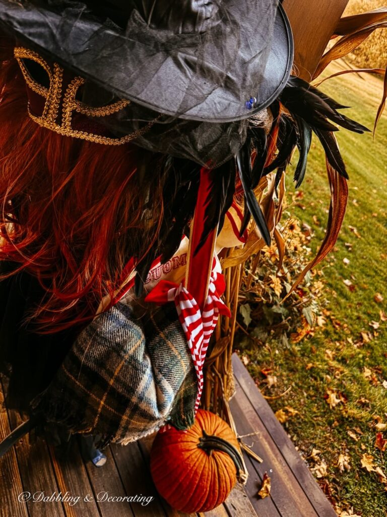 Close up of mannequin witch on Halloween porch with accessories like stockings, mask, red wig, feathered collar, witch's hat.