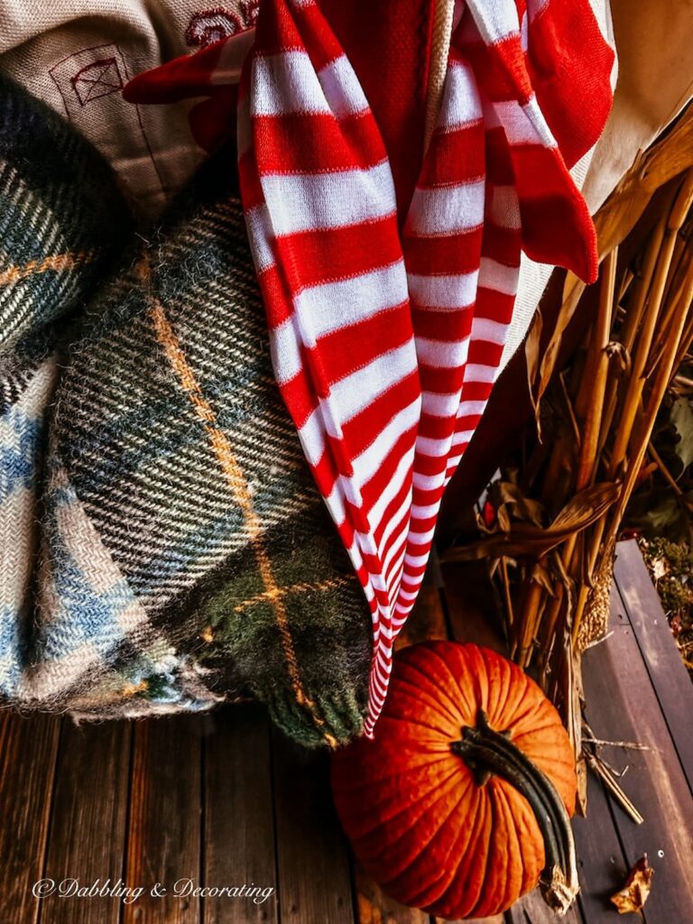 red and white striped witch's stockings and a plaid blanket in bag with a pumpkin on porch flooring close up photo.