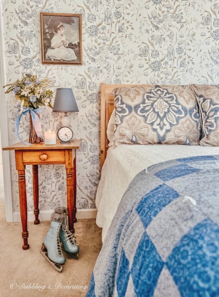 Guest bedroom in Vermont styled with an old sleigh bed, and an antique wooden side table with Hayden Rowe's First Tracks candle burning and vintage blue ice skates at the table's legs.