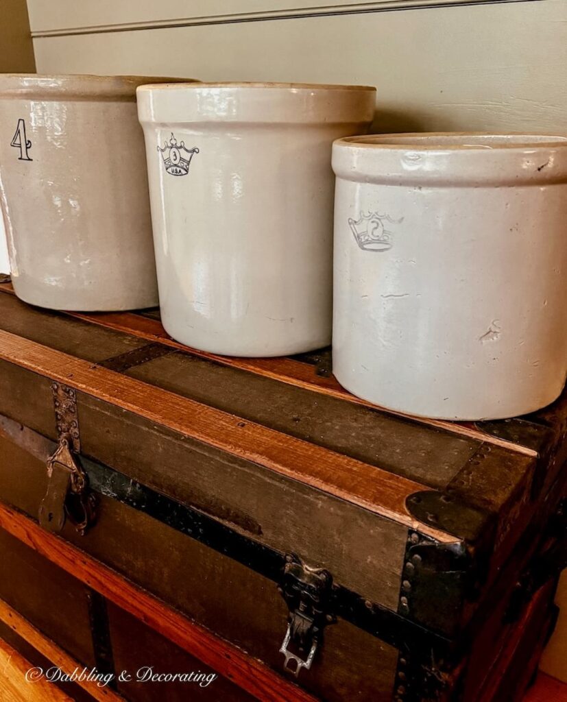 three empty vintage crocks in different sizes on an antique trunk