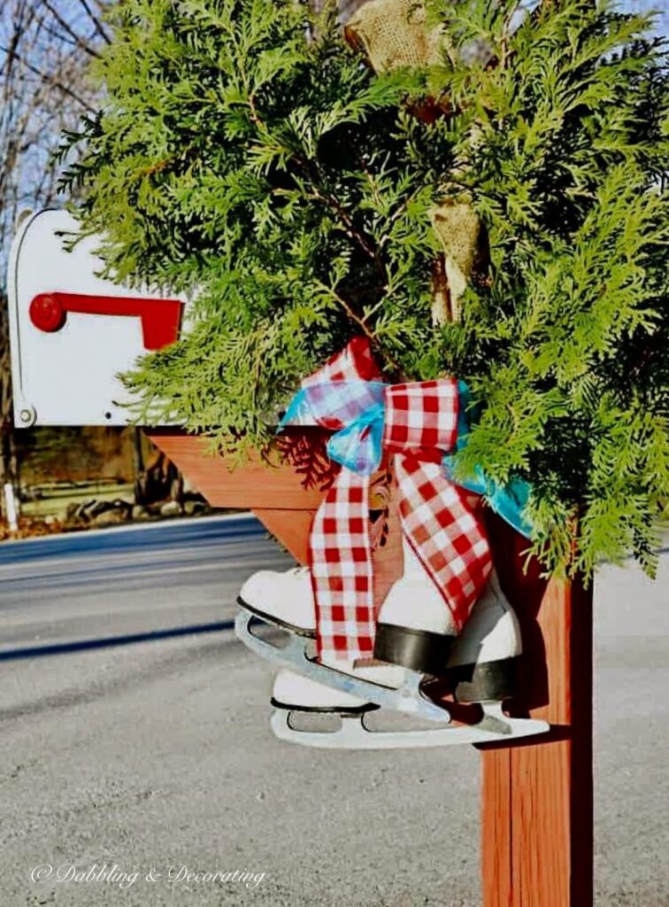 A pair of white vintage ice skates hanging from a winter mailbox with gingham red and white and blue bow with large bouquet of evergreens.