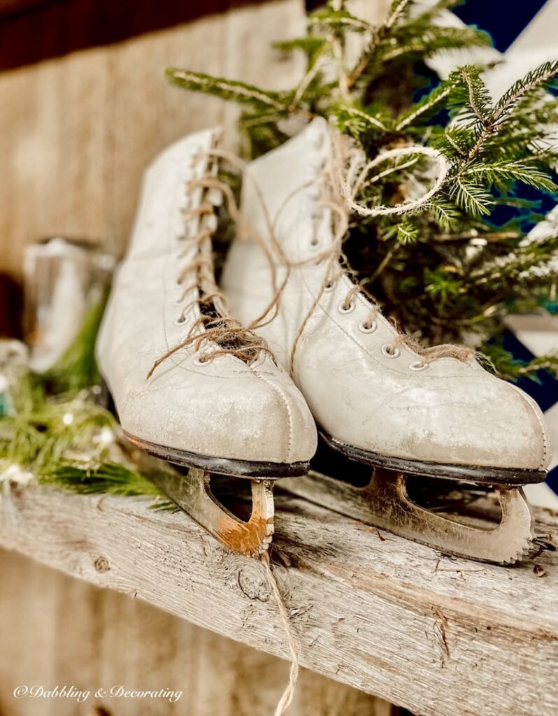 Pair of white vintage ice skates decoration with evergreens on rustic wood mantel with jute twine as lacings.