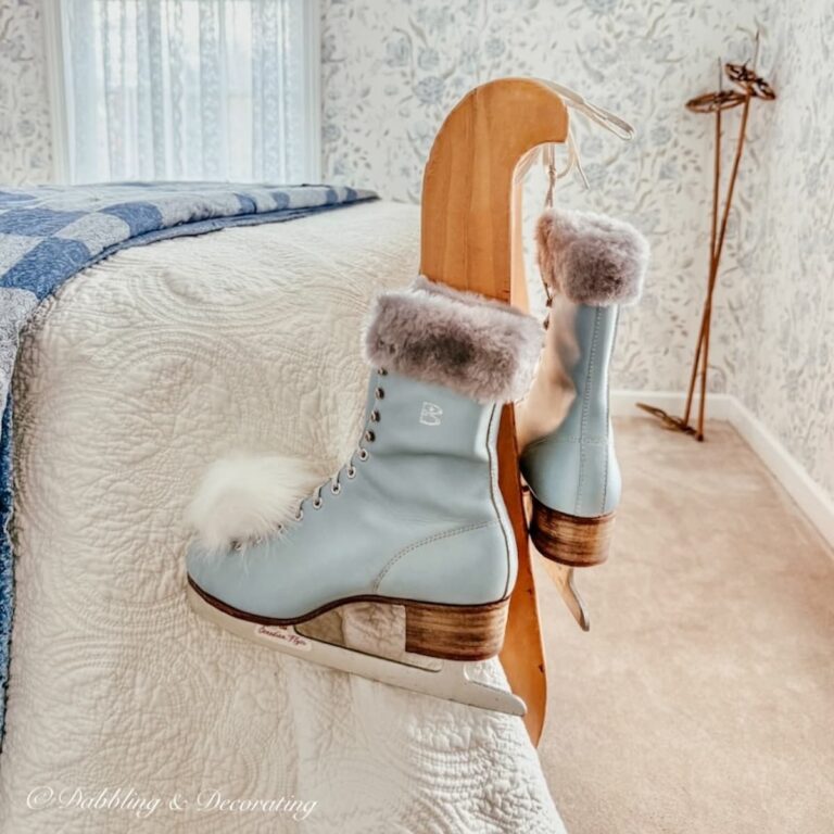 A pair of vintage Canadian Flyers blue ice skates with fur on ankles hanging from side of sleigh bed with white furry pom poms on the toes.
