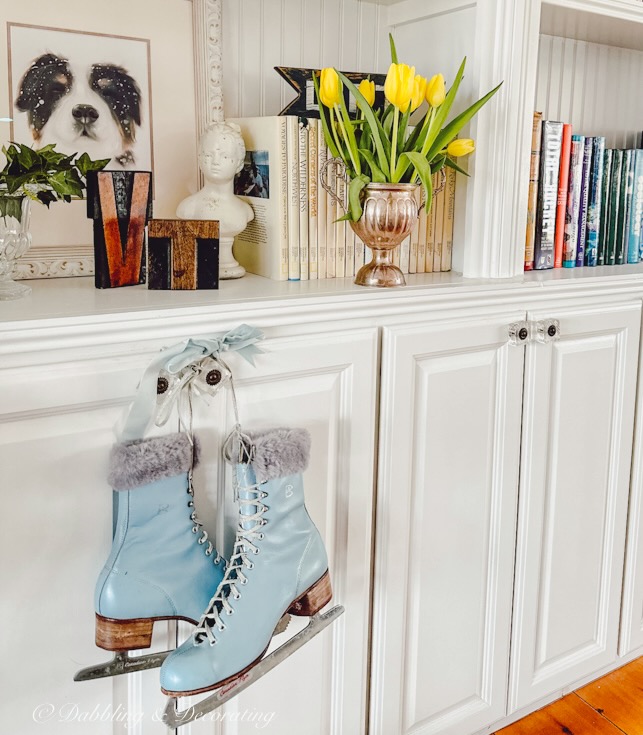 Vintage ice skates decoration with blue skates hanging on built-in shelving knob paired with yellow tulips in vintage trophy on bookshelves with books for spring.