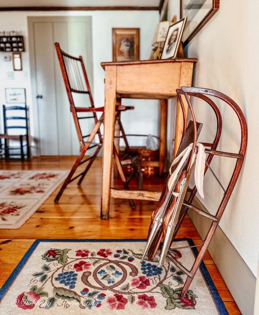 Antique wooden sled with antique racing ice skates displayed next to a large vintage desk and chair for Christmas decoration.